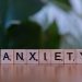 Close-up of wooden blocks spelling ANXIETY on a wooden surface with blurred green background.