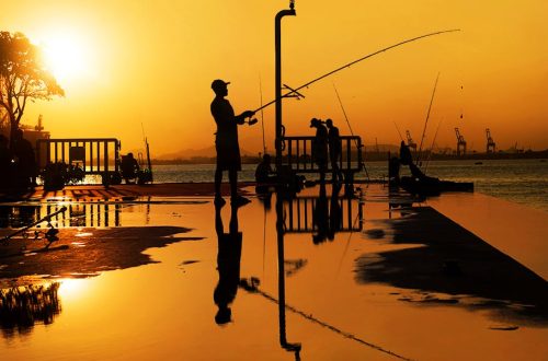 Fishermen cast silhouettes against a glowing orange sunset in Rio de Janeiro, creating a serene and reflective scene.