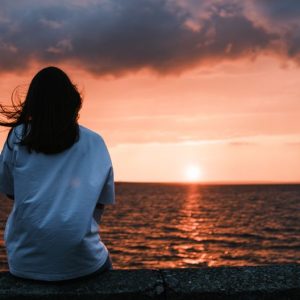 Tranquil evening scene with a woman gazing at a stunning sunset over the ocean, capturing a moment of serenity.