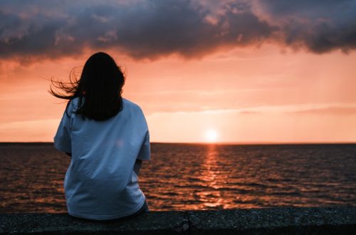 Tranquil evening scene with a woman gazing at a stunning sunset over the ocean, capturing a moment of serenity.