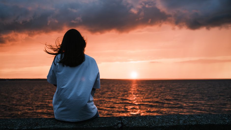 Tranquil evening scene with a woman gazing at a stunning sunset over the ocean, capturing a moment of serenity.