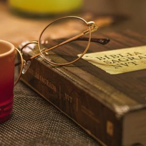 A Biblia Sagrada with glasses rests on a table beside a red mug, symbolizing relaxation and reflection.
