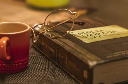 A Biblia Sagrada with glasses rests on a table beside a red mug, symbolizing relaxation and reflection.