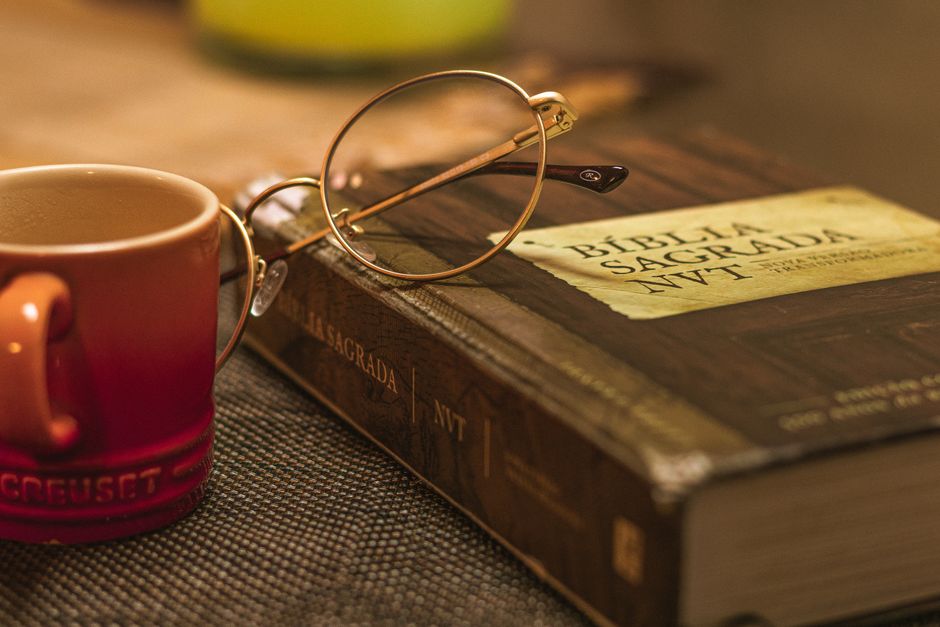 A Biblia Sagrada with glasses rests on a table beside a red mug, symbolizing relaxation and reflection.