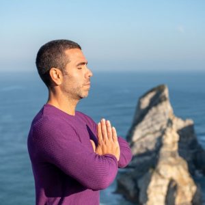 Side view of a man meditating by the ocean cliffs in Portugal, promoting relaxation and mindfulness.