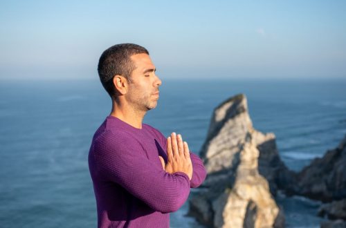 Side view of a man meditating by the ocean cliffs in Portugal, promoting relaxation and mindfulness.