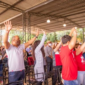 Outdoor gathering with diverse crowd raising arms in excitement under a canopy.
