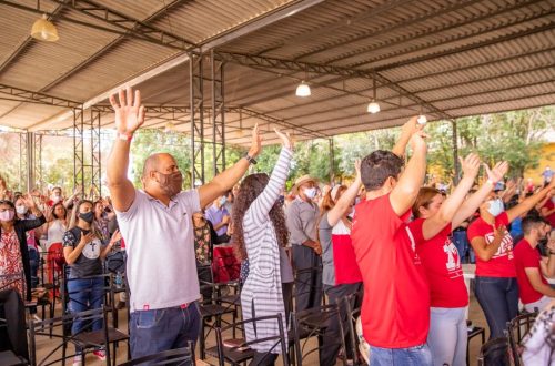 Outdoor gathering with diverse crowd raising arms in excitement under a canopy.