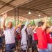 Outdoor gathering with diverse crowd raising arms in excitement under a canopy.