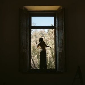 Silhouette of a person standing in a window frame overlooking nature. Captures solitude and reflection.