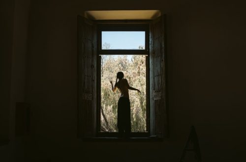 Silhouette of a person standing in a window frame overlooking nature. Captures solitude and reflection.