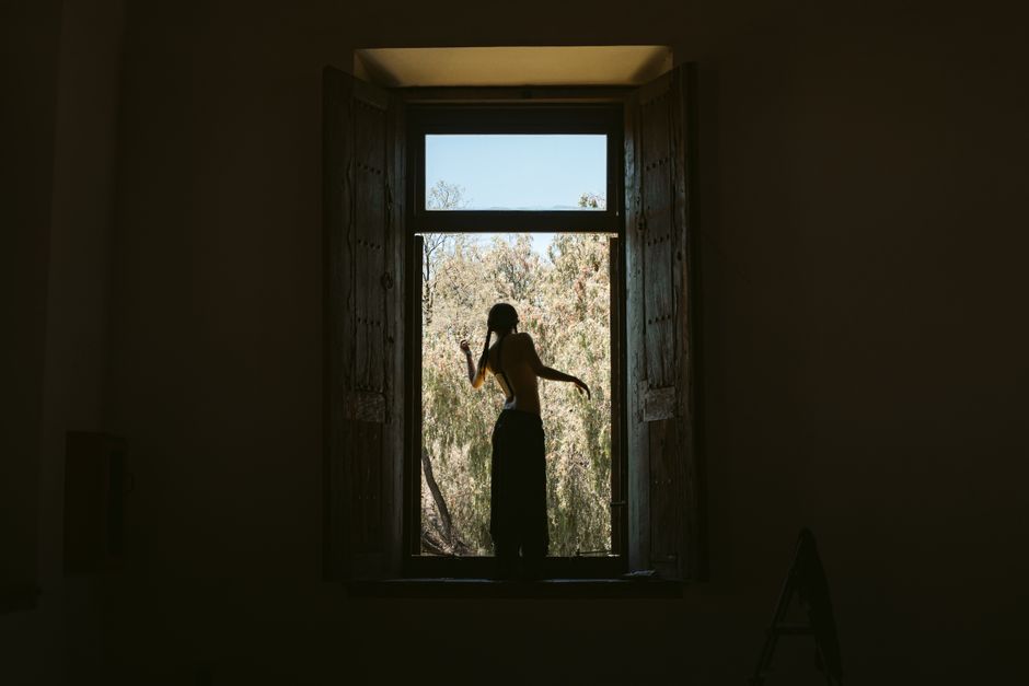 Silhouette of a person standing in a window frame overlooking nature. Captures solitude and reflection.