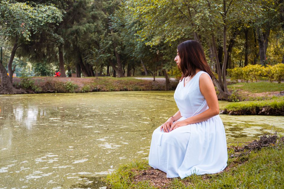 A woman in a white dress kneels by a serene pond in Tlaxcala de Xicohténcatl, México.