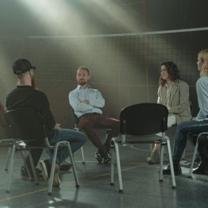 A group therapy session with six adults seated in a circle, discussing support and mental health.