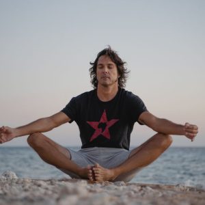 A serene image of a man practicing meditation on a beach, embracing tranquility at the seashore during sunset.