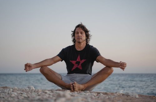 A serene image of a man practicing meditation on a beach, embracing tranquility at the seashore during sunset.