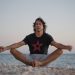 A serene image of a man practicing meditation on a beach, embracing tranquility at the seashore during sunset.