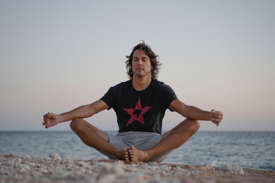 A serene image of a man practicing meditation on a beach, embracing tranquility at the seashore during sunset.
