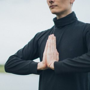 Close-up of a person meditating outdoors with hands in prayer position, promoting wellness.