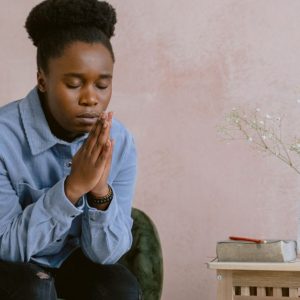 A woman in quiet contemplation, praying with hands clasped, embodying faith and serenity.