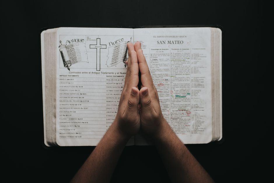 Hands clasped in prayer on an open Bible showing the book of Matthew, emphasizing faith and spirituality.