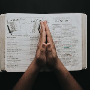 Hands clasped in prayer on an open Bible showing the book of Matthew, emphasizing faith and spirituality.