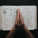 Hands clasped in prayer on an open Bible showing the book of Matthew, emphasizing faith and spirituality.
