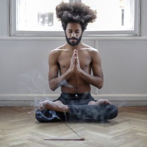 Shirtless man meditating in lotus pose indoors with incense smoke creating a serene atmosphere.