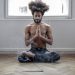Shirtless man meditating in lotus pose indoors with incense smoke creating a serene atmosphere.