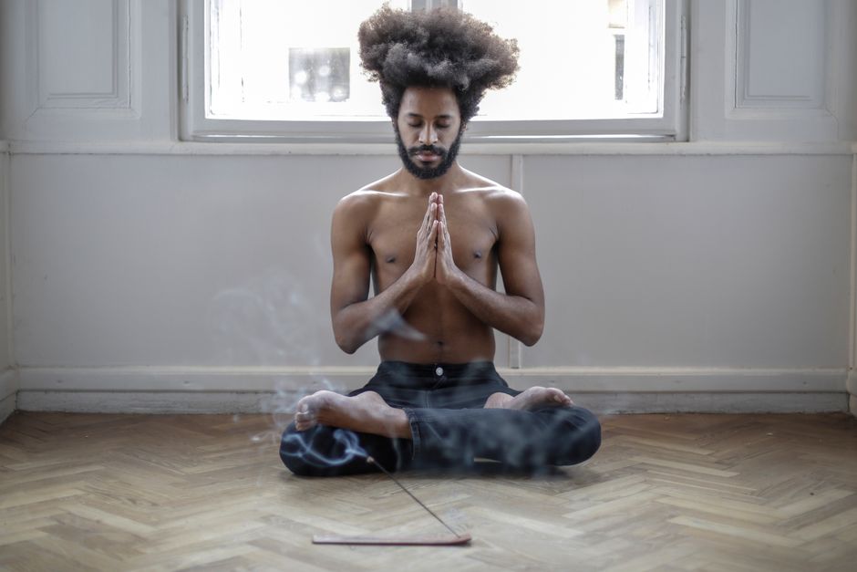 Shirtless man meditating in lotus pose indoors with incense smoke creating a serene atmosphere.