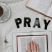 Flat lay of morning prayer routine including Bible, coffee, and 'PRAY' letters.