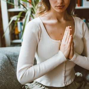A woman practicing meditation indoors, focusing with hands in prayer position.
