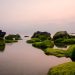 Tranquil seascape with mossy rocks in calm waters under a pink sunset sky.