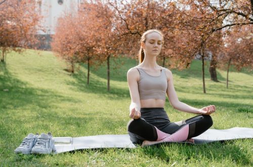 A woman practicing meditation on a yoga mat in a tranquil park setting during springtime.