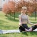 A woman practicing meditation on a yoga mat in a tranquil park setting during springtime.