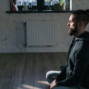 Side view of a man meditating indoors in a serene environment, promoting mental wellness and tranquility.