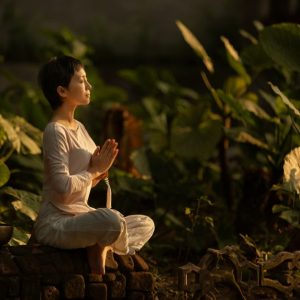 Serene scene of a woman meditating in a lush garden setting at daylight.