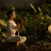 Serene scene of a woman meditating in a lush garden setting at daylight.
