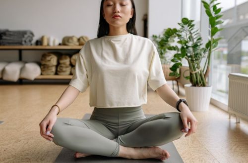 Woman sitting cross-legged on a yoga mat indoors, eyes closed, conveying peace and relaxation.