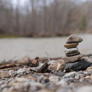 A stack of stones beautifully balanced on a rocky riverbank with a blurred forest background.