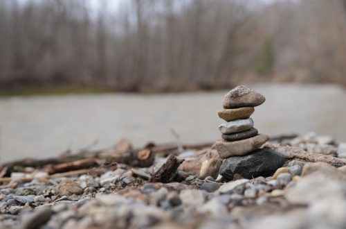 A stack of stones beautifully balanced on a rocky riverbank with a blurred forest background.