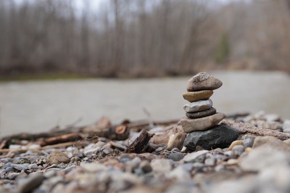 A stack of stones beautifully balanced on a rocky riverbank with a blurred forest background.
