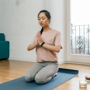 A woman practicing meditation and relaxation indoors on a yoga mat, promoting a healthy lifestyle.