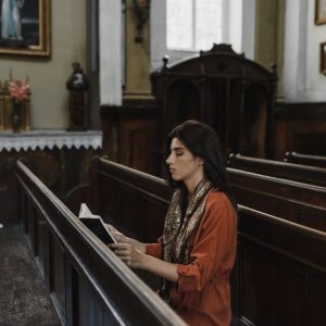 A woman sits and prays in a peaceful and historic church adorned with religious art.