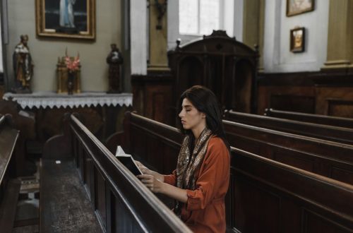 A woman sits and prays in a peaceful and historic church adorned with religious art.