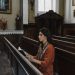 A woman sits and prays in a peaceful and historic church adorned with religious art.