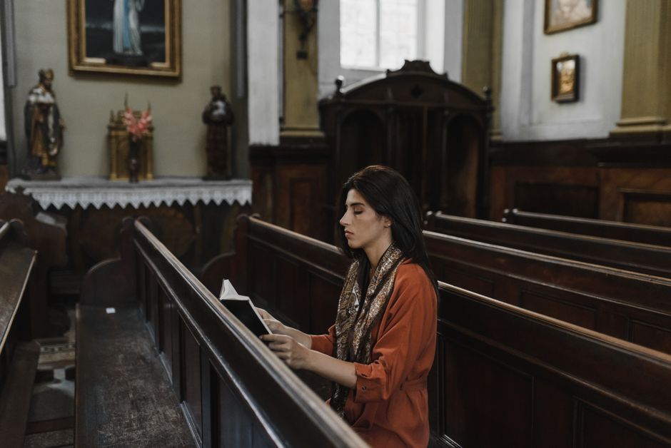 A woman sits and prays in a peaceful and historic church adorned with religious art.