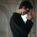 A man solemnly praying with a rosary in a serene church setting, side profile view.