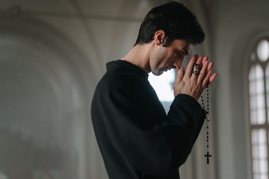 A man solemnly praying with a rosary in a serene church setting, side profile view.