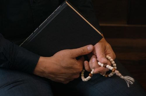 Close-up of hands holding prayer beads and book, symbolizing faith and spirituality.
